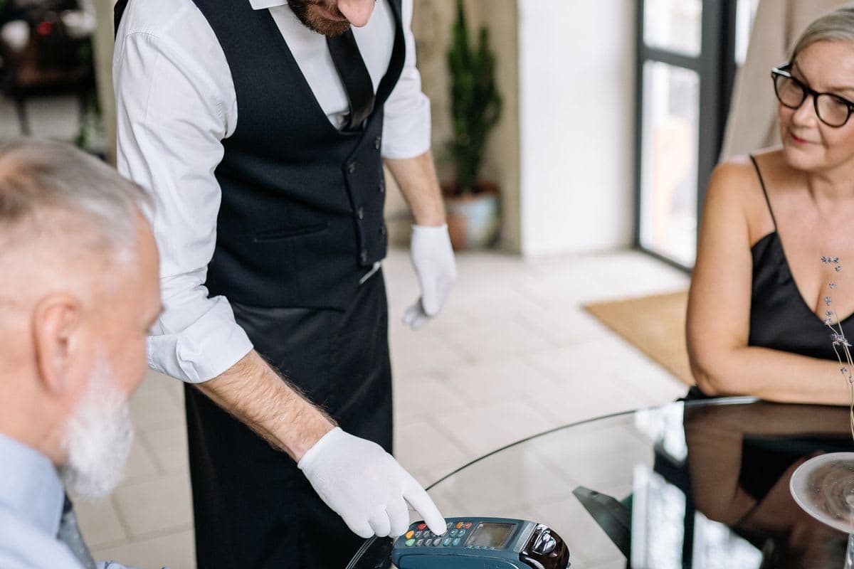 Kellner hält Gästen im Restaurant ein Kartenterminal zur Zahlung hin