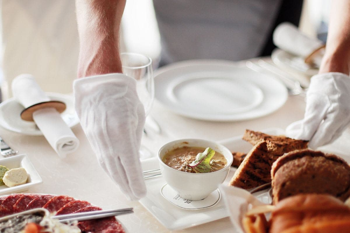 Kellner serviert Speisen an einem eingedeckten Restauranttisch